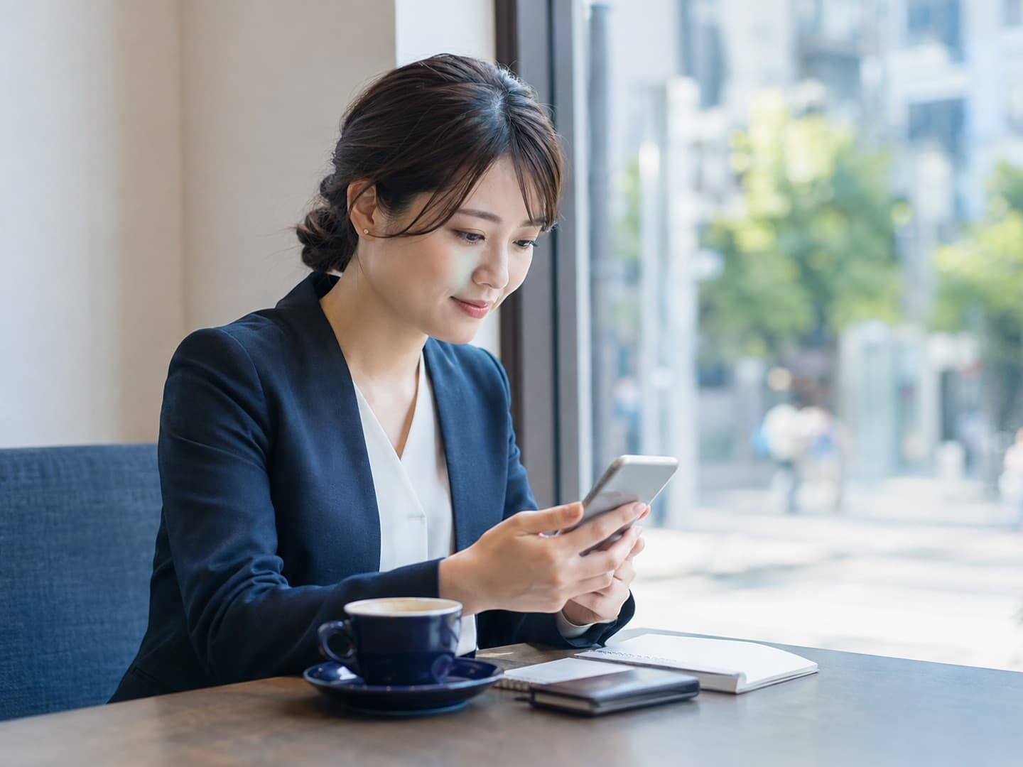 カフェでスマホを見ながら訪問前の準備をしている女性の営業担当